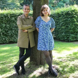 Portrait of Maarten Slagboom and Billie Slagboom, standing either side of a tree trunk in a sunlit garden.