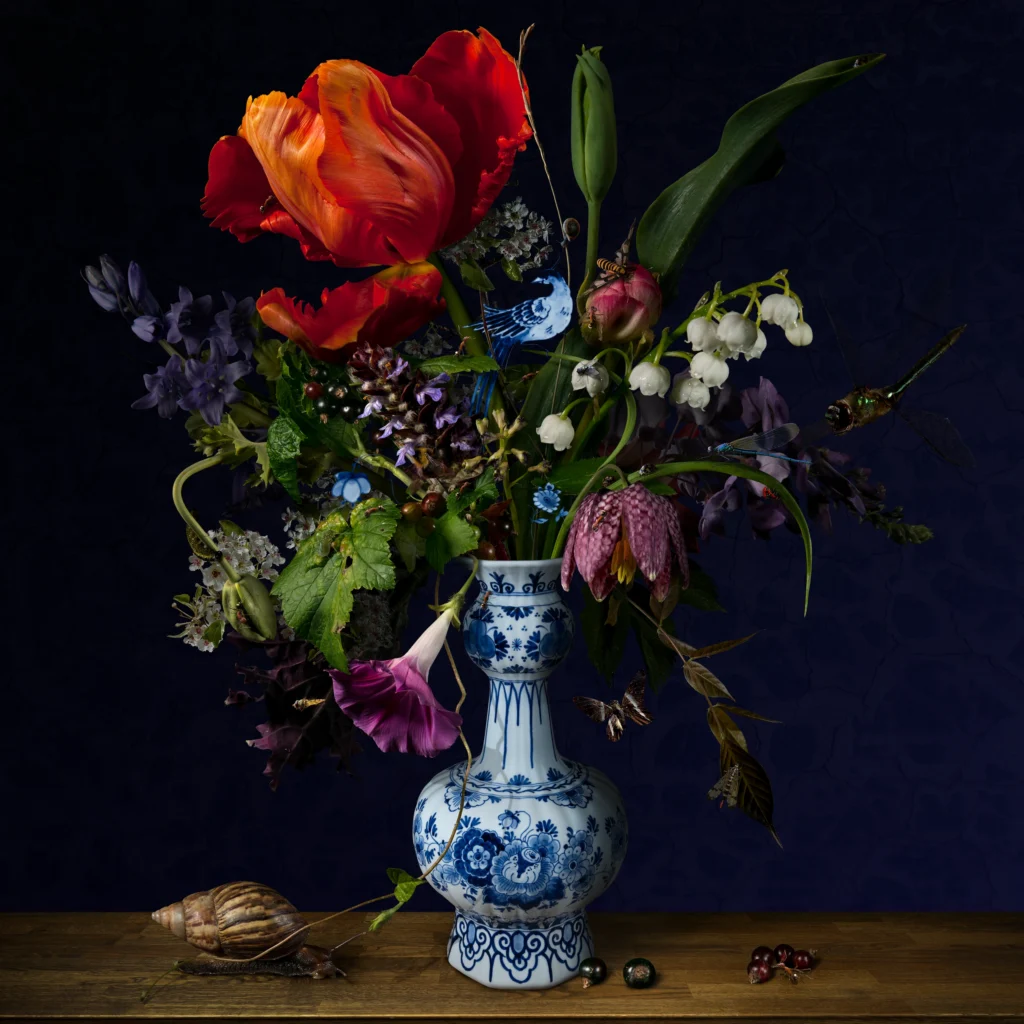 A dark, moody bouquet with a large red parrot tulip, lily of the valley and a snake’s head fritillary in a bulbous Delft blue vase.