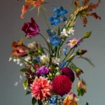 Dahlias, tulips, gloriosa and blue delphinium in a small Delft blue vase, with a butterfly hovering above.