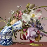 A fallen Delft blue Blow Away vase with a bouquet of tulips, lilies and peonies lying on a wooden table, with butterflies.