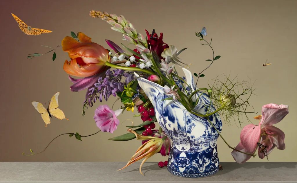 A toppled Delft blue Blow Away vase with tulips and lilies spilling across a table, with yellow butterflies.