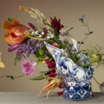 A toppled Delft blue Blow Away vase with tulips and lilies spilling across a table, with yellow butterflies.