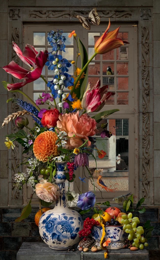 A bouquet of tulips, iris and roses in a Delft blue vase before a window, with grapes and fruit on the ledge.