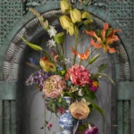 Tulips, roses and pink lilies in a Delft blue vase set in a weathered green-stone niche.