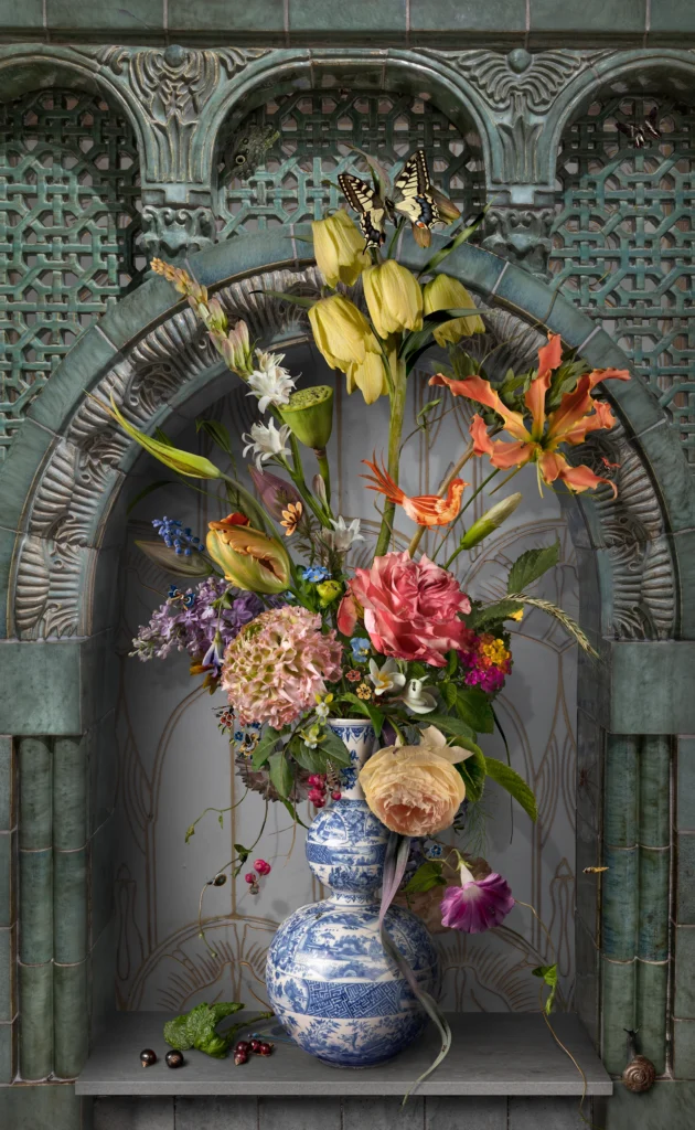 Tulips, roses and pink lilies in a Delft blue vase set in a weathered green-stone niche.