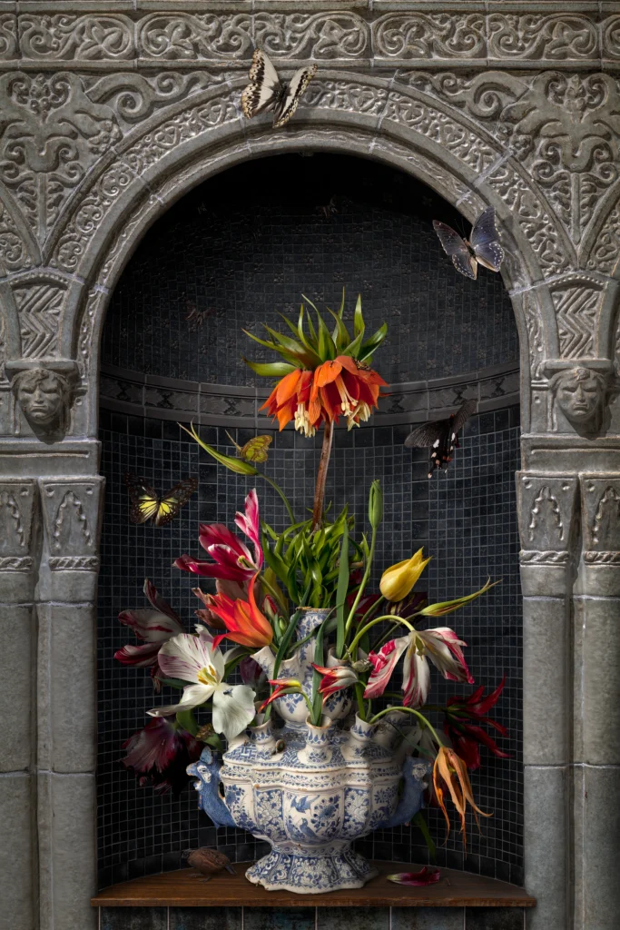 A Delft blue flower pyramid filled with tulips and a crown imperial in a carved stone niche.