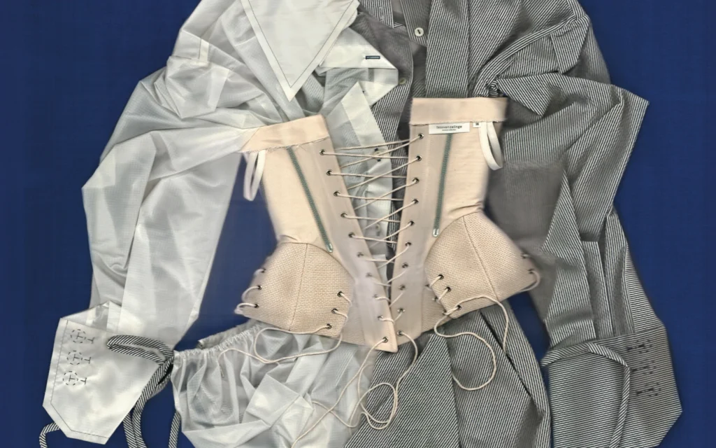 PAN Amsterdam 2026 campaign image by Tess van Zalinge: a traditional corset laced over white and grey shirts on a deep blue ground