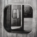 Close view of a rounded rectangular concrete window set into a striped concrete wall, framing a second rounded window inside it.