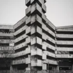 Stepped tower of stacked concrete slabs rising above a low block, with a zebra crossing in the foreground.