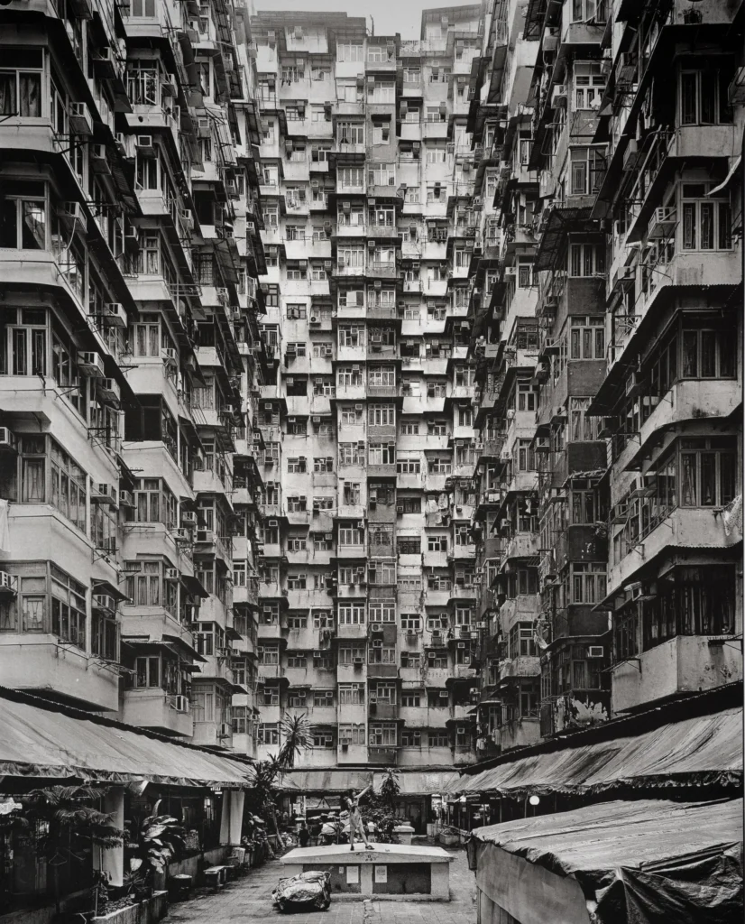A narrow courtyard between tall apartment façades of stacked balconies, seen from street level with market stalls below.