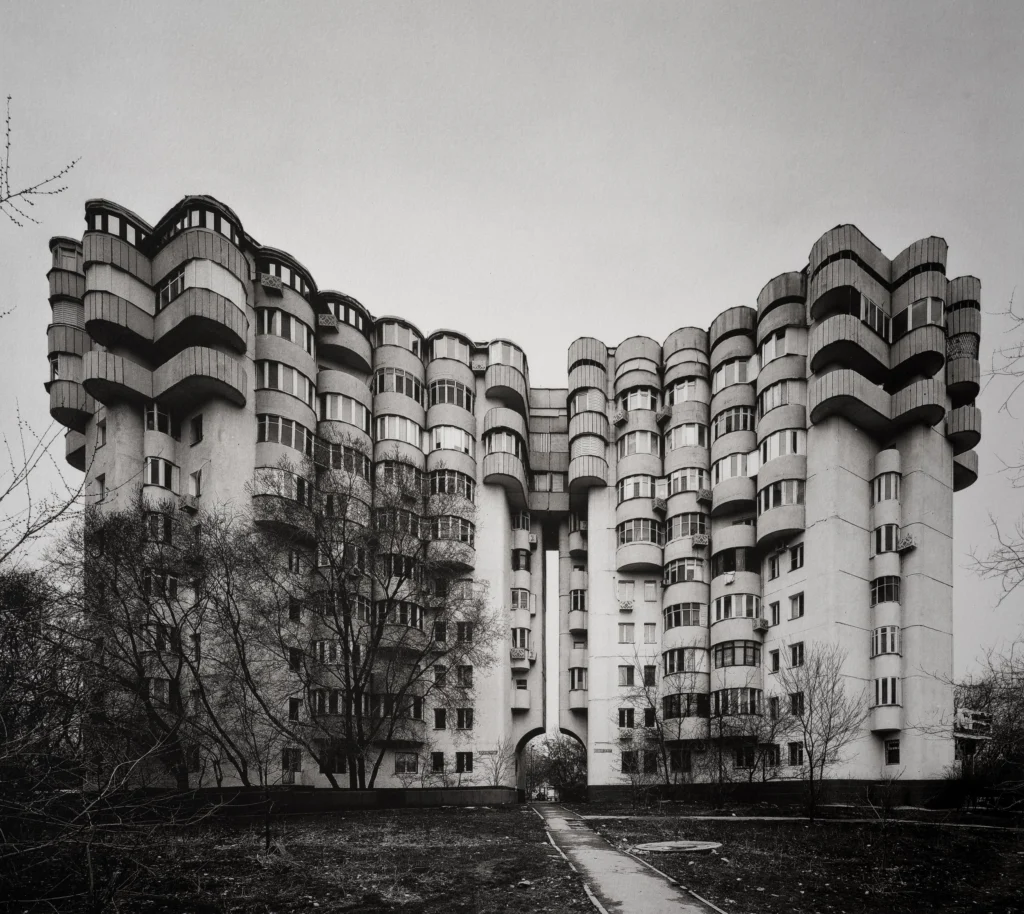 A long residential block with rounded balcony stacks and turret-like corners, set behind bare trees.