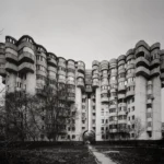 A long residential block with rounded balcony stacks and turret-like corners, set behind bare trees.